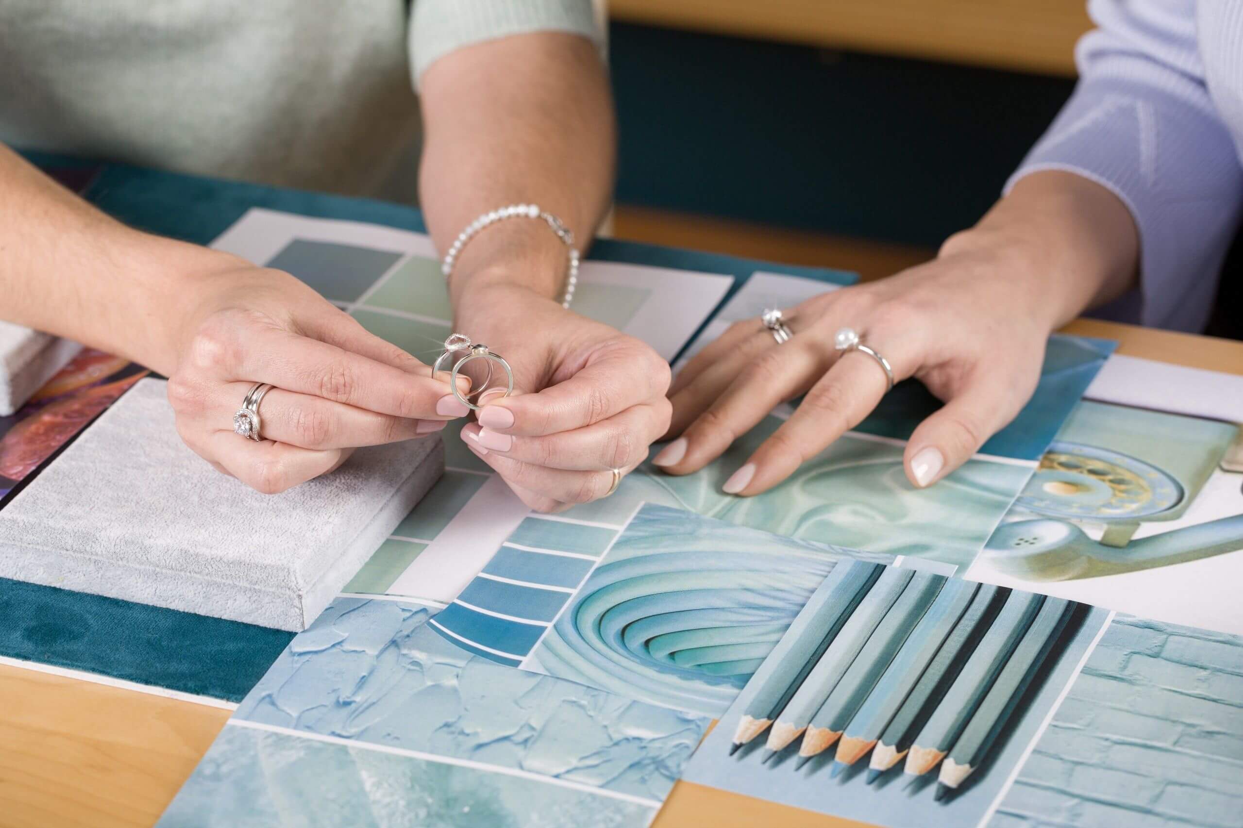 A team of designers examines UNIKE rings on a table with a mood board in shades of blue and green, reflecting the care taken in every detail. The team of designers carefully selected the pantone of each box that accompanies these sterling silver rings wit